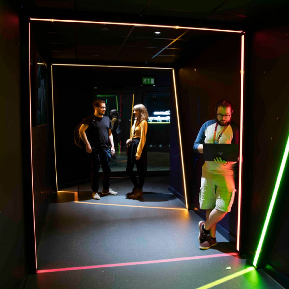 Three people standing in a dark space framed by lines of light